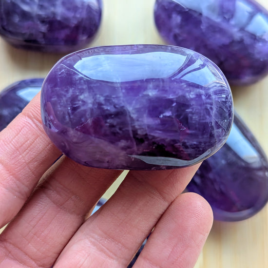 Purple gemstone held in a hand with more gemstones in the background on a light surface