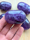 Purple gemstone held in a hand with more gemstones in the background on a light surface