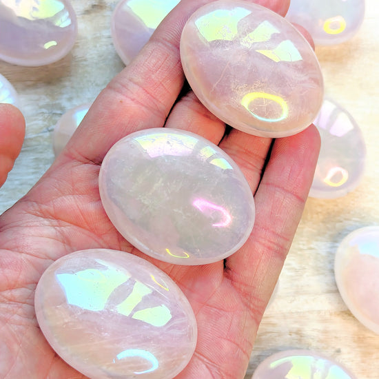 Hand holding Angel Aura Rose Quartz Palm stones with a blurred background