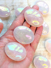 Hand holding Angel Aura Rose Quartz Palm stones with a blurred background