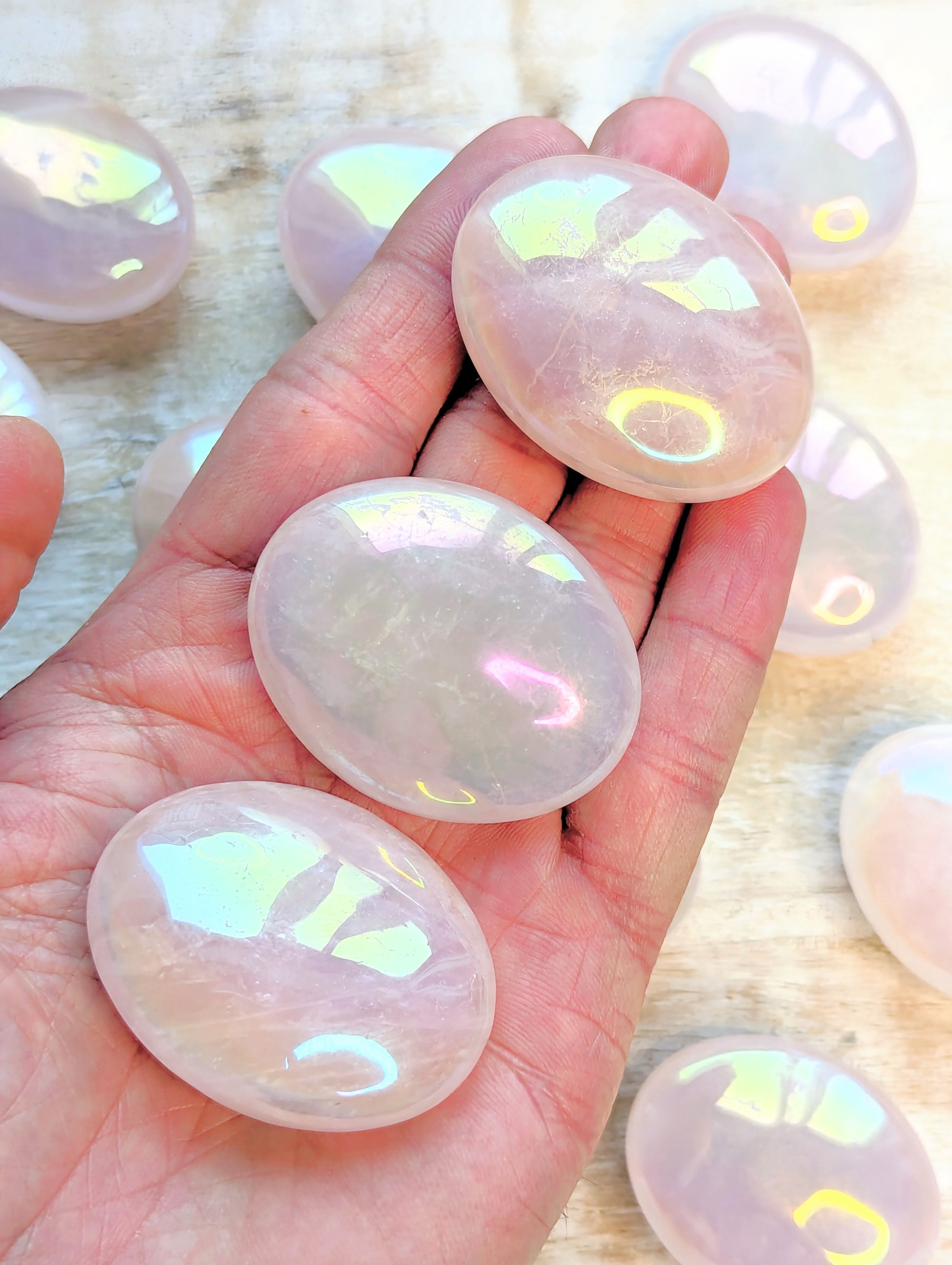 Hand holding Angel Aura Rose Quartz Palm stones with a blurred background