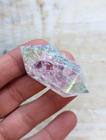 Angel Aura Quartz Wand Double Point held in a hand with a blurred background