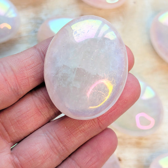 Iridescent Angel Aura Rose Quartz Palm Stone crystal held in a hand with blurred colorful background