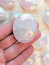 Iridescent Angel Aura Rose Quartz Palm Stone crystal held in a hand with blurred colorful background