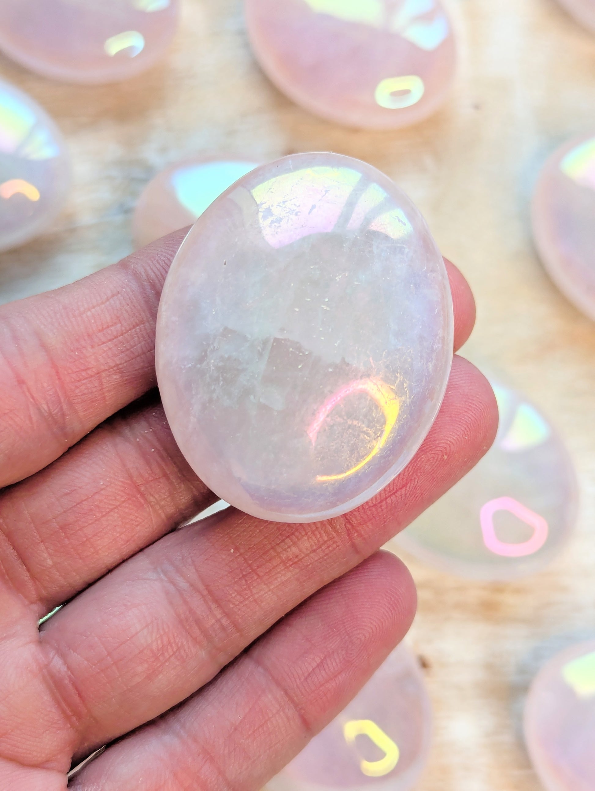 Iridescent Angel Aura Rose Quartz Palm Stone crystal held in a hand with blurred colorful background