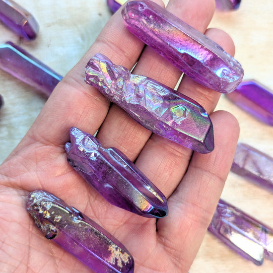 Hand holding angel aura purple quartz point and iridescent nail art designs on nails with a blurred background.