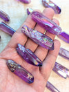 Hand holding angel aura purple quartz point and iridescent nail art designs on nails with a blurred background.