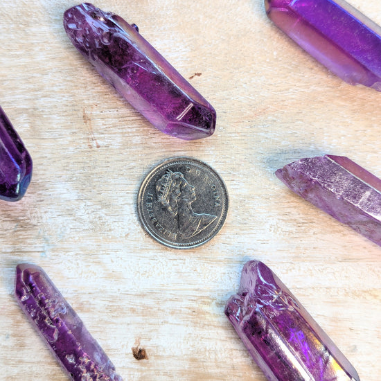 Angel Aura Purple crystal points on a wooden surface with a coin for scale.