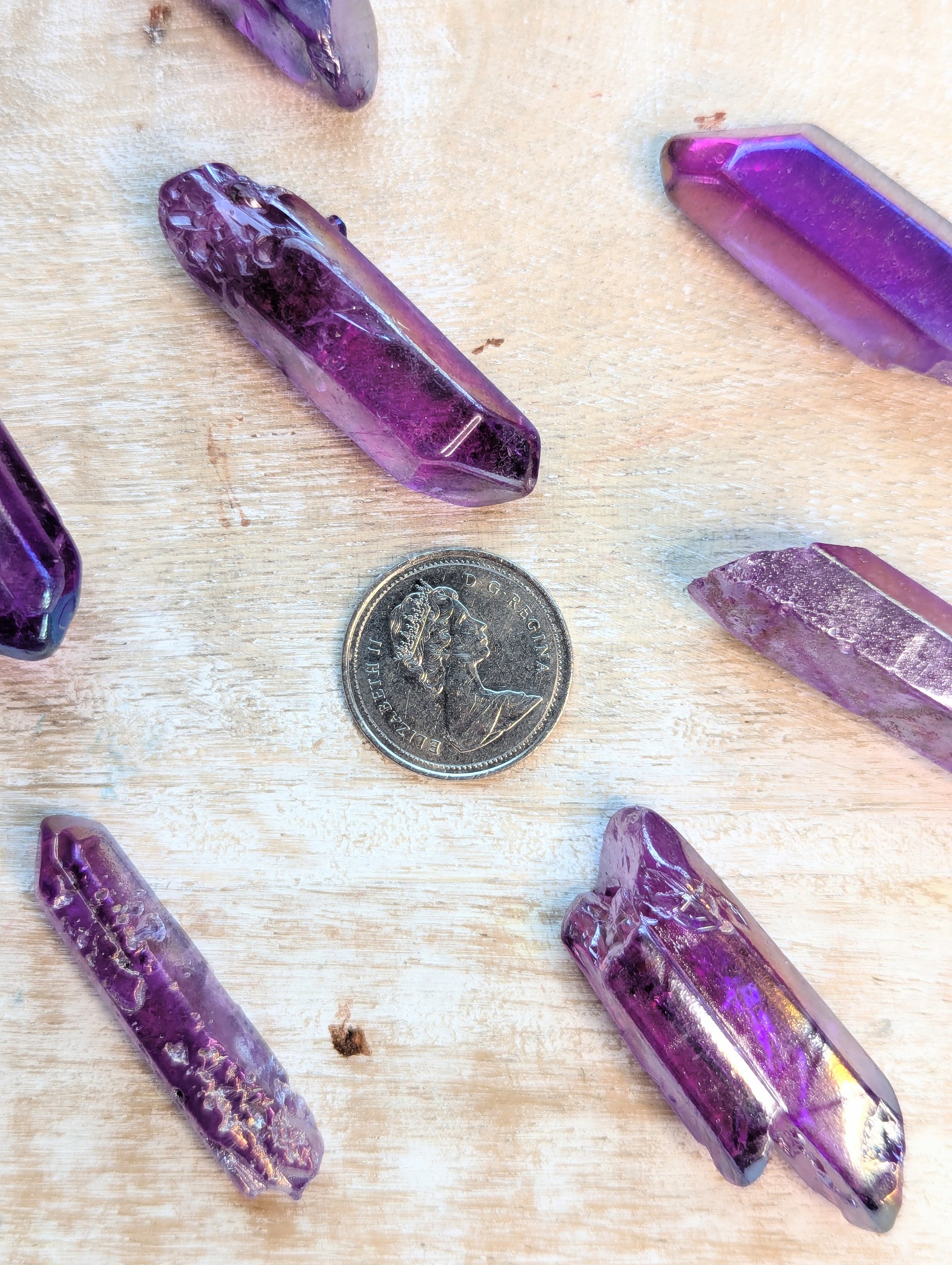 Angel Aura Purple crystal points on a wooden surface with a coin for scale.