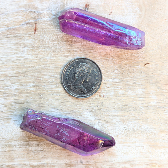 Two angel aura purple crystals on a wooden surface with a coin for scale.