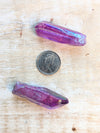Two angel aura purple crystals on a wooden surface with a coin for scale.