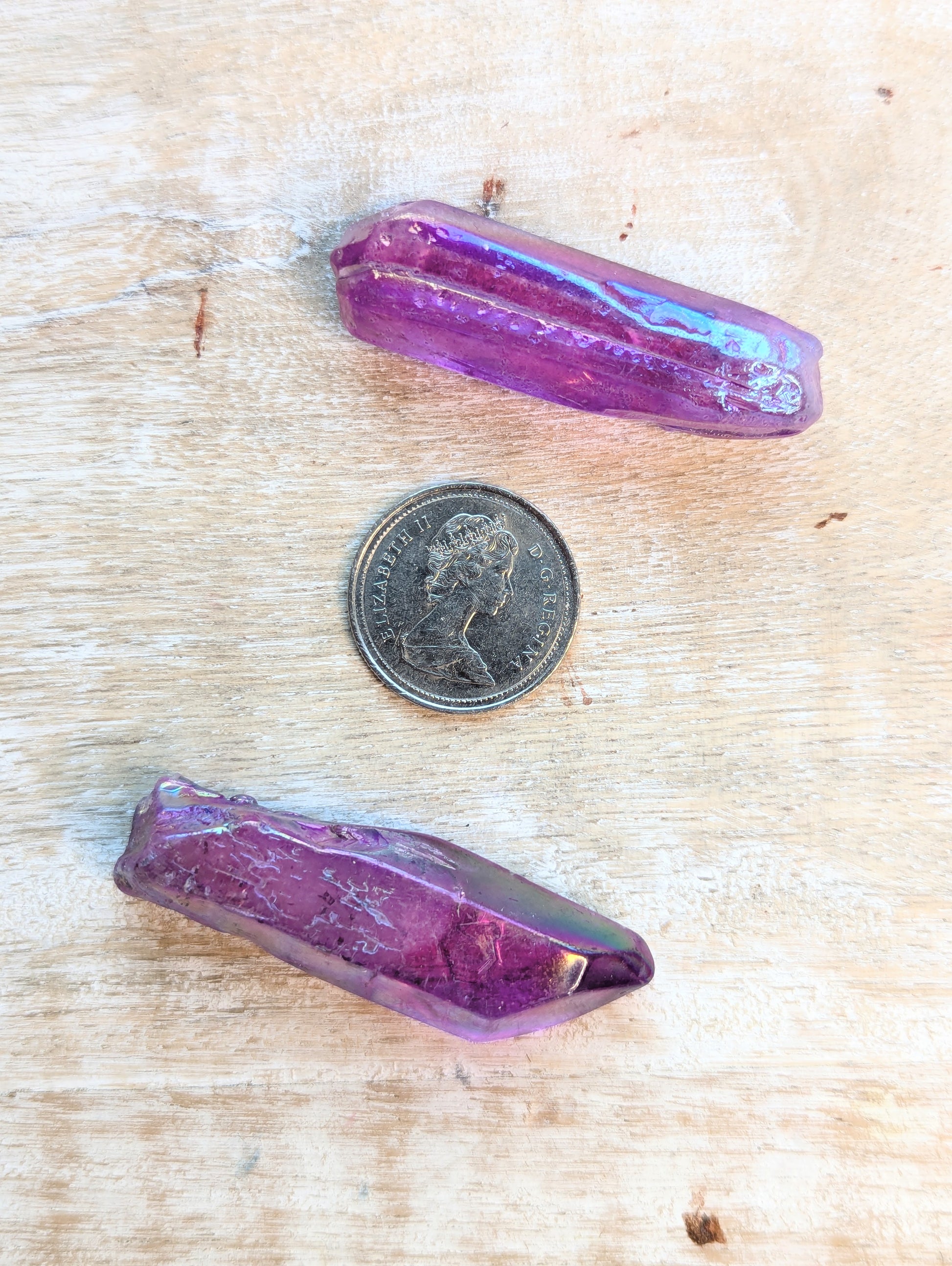 Two angel aura purple crystals on a wooden surface with a coin for scale.