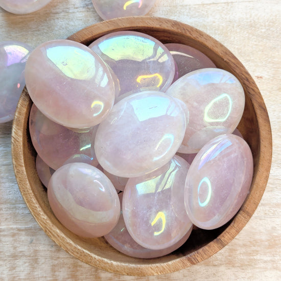 Aura Rose Quartz Palm stones in a wooden bowl on a light wood surface