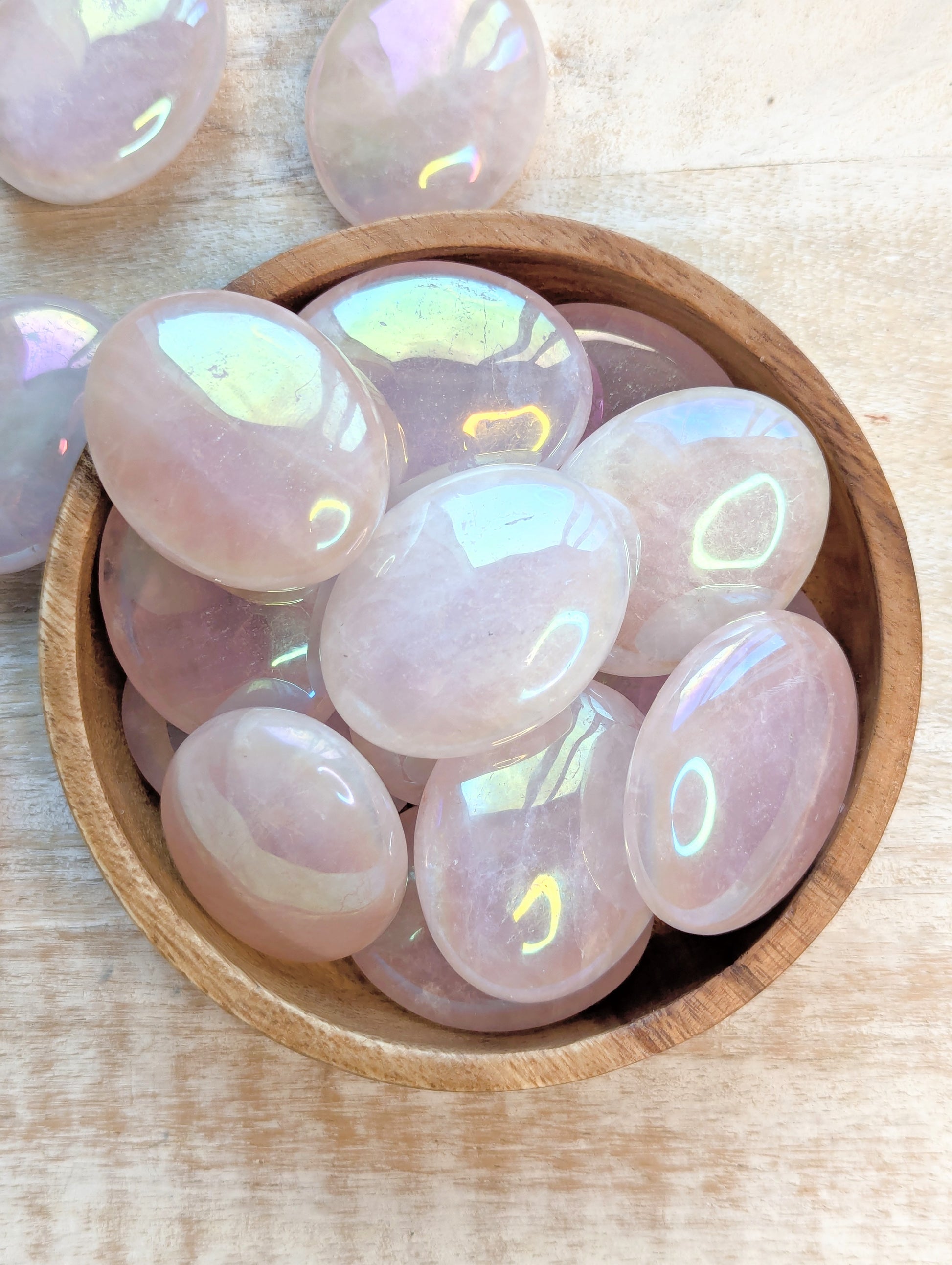 Aura Rose Quartz Palm stones in a wooden bowl on a light wood surface