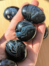 Black onyx stones held in a hand on a wooden surface