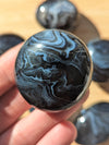 Close-up of a black onyxstone held in a hand with more stones in the background.