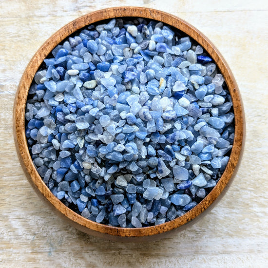 Wooden bowl filled with blue aventurine crystal chips on a light wooden surface
