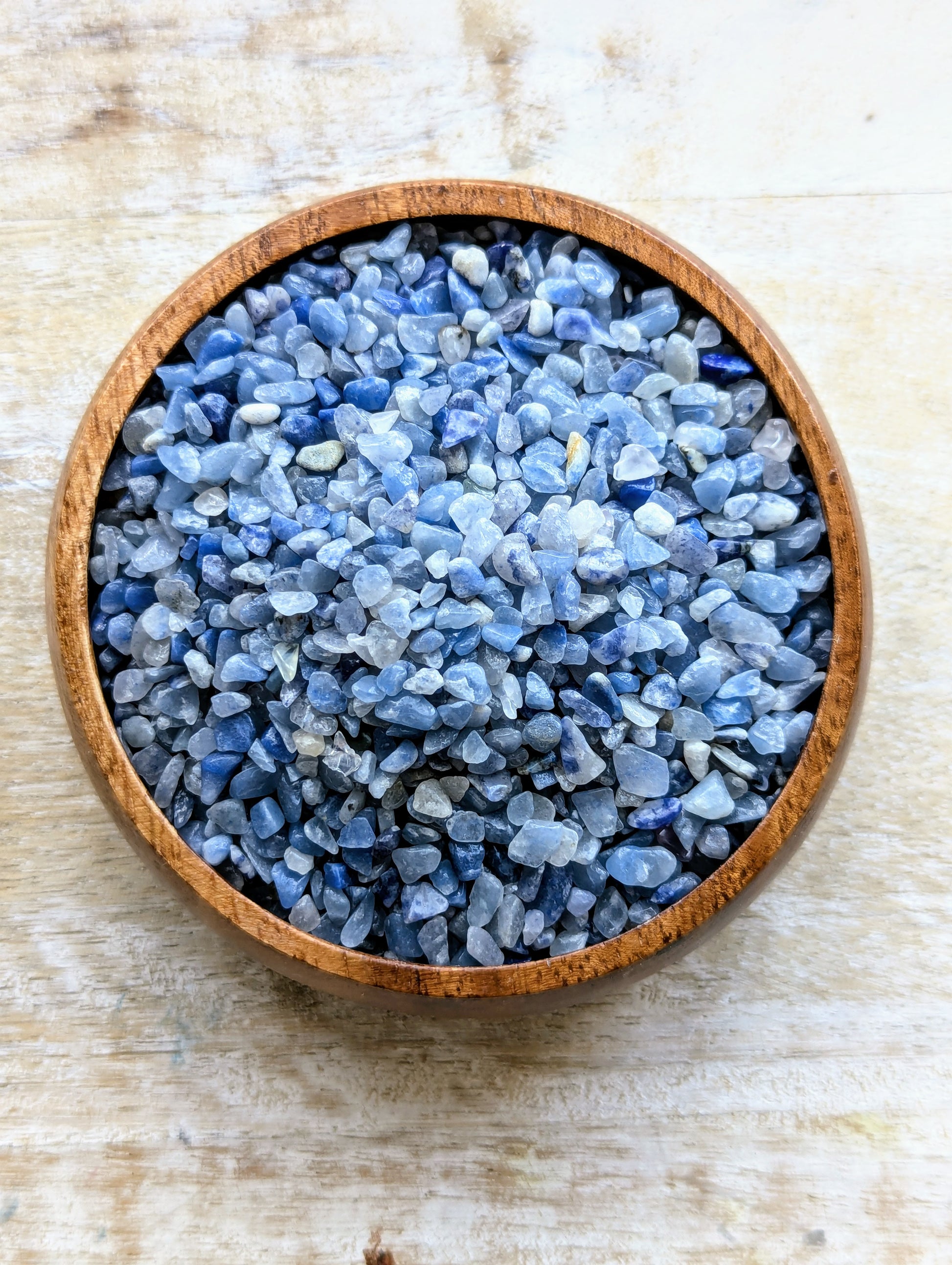 Wooden bowl filled with blue aventurine crystal chips on a light wooden surface