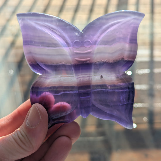 Butterfly-shaped object with purple and pink gradient held by a hand against a blurred background