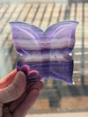 Butterfly-shaped object with purple and pink gradient held by a hand against a blurred background