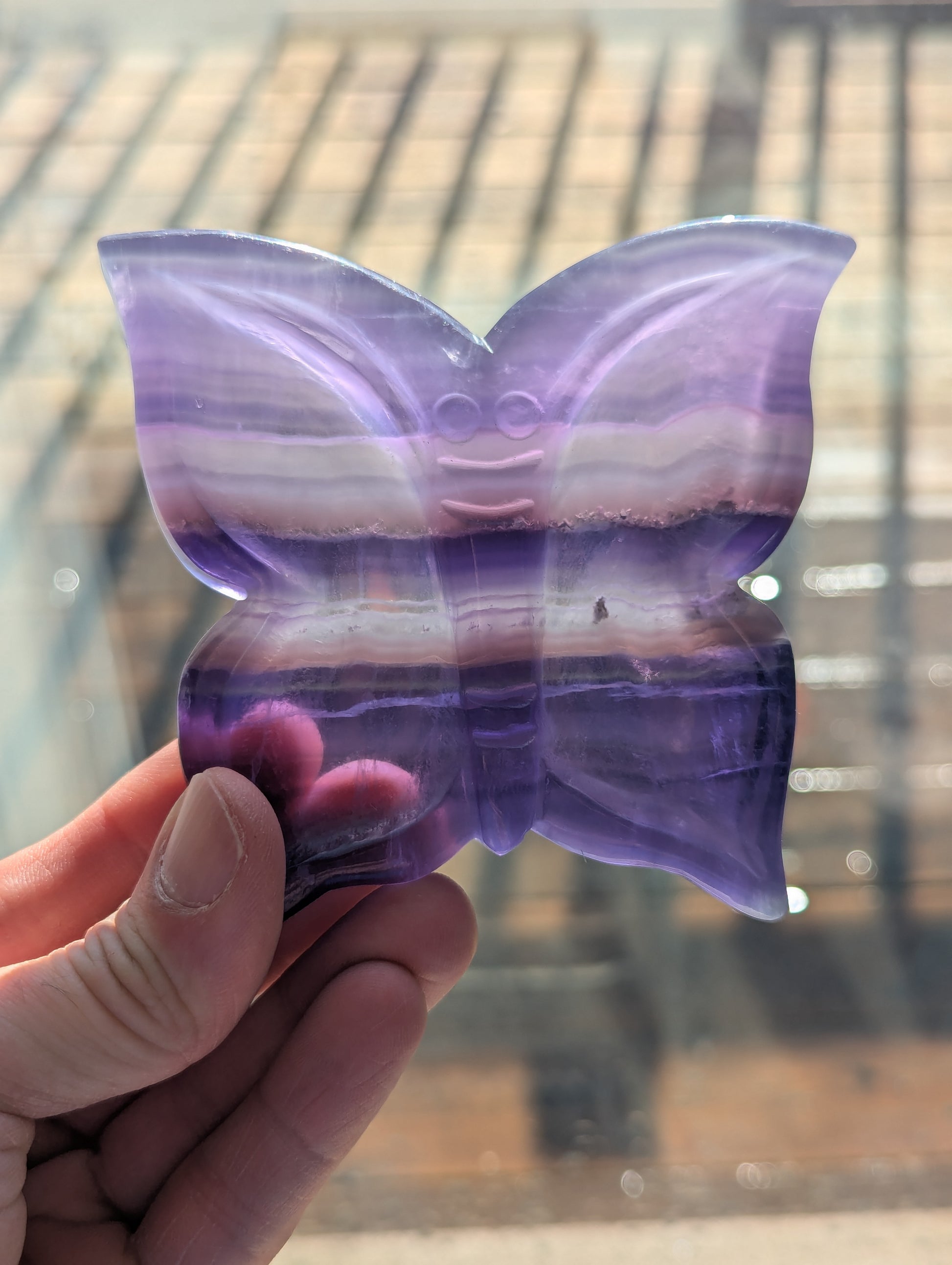 Butterfly-shaped object with purple and pink gradient held by a hand against a blurred background
