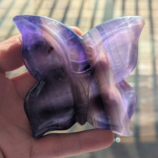 Butterfly-shaped object with purple and clear sections held in a hand against a blurred background