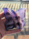 Butterfly-shaped object with purple and clear sections held in a hand against a blurred background