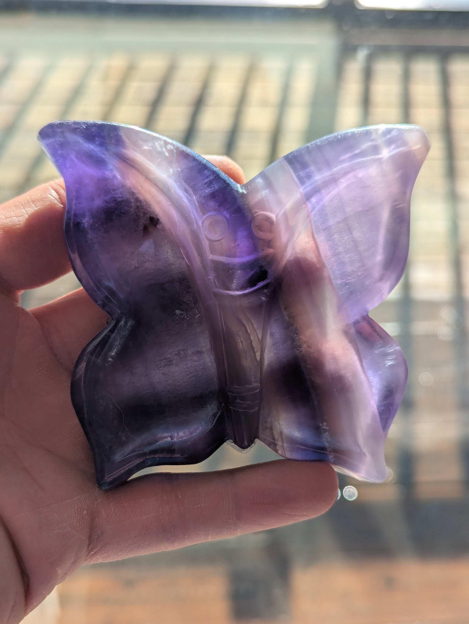 Butterfly-shaped object with purple and clear sections held in a hand against a blurred background