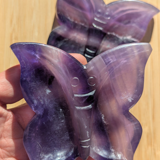 Purple butterfly-shaped objects held in a hand on a wooden surface