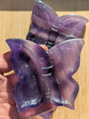 Purple butterfly-shaped objects held in a hand on a wooden surface