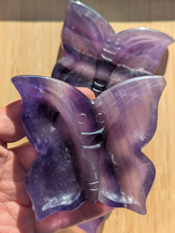 Purple butterfly-shaped objects held in a hand on a wooden surface
