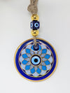 A circular evil eye (Nazar) wall hanging ornament with a blue and white geometric pattern, gold trim, and a beige jute rope with decorative blue and gold beads at the top, shown on a plain white background.