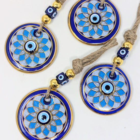 Three matching circular evil eye wall hanging with blue and white enamel patterns, gold-plated borders, and brown cord tassels, displayed on a white background.