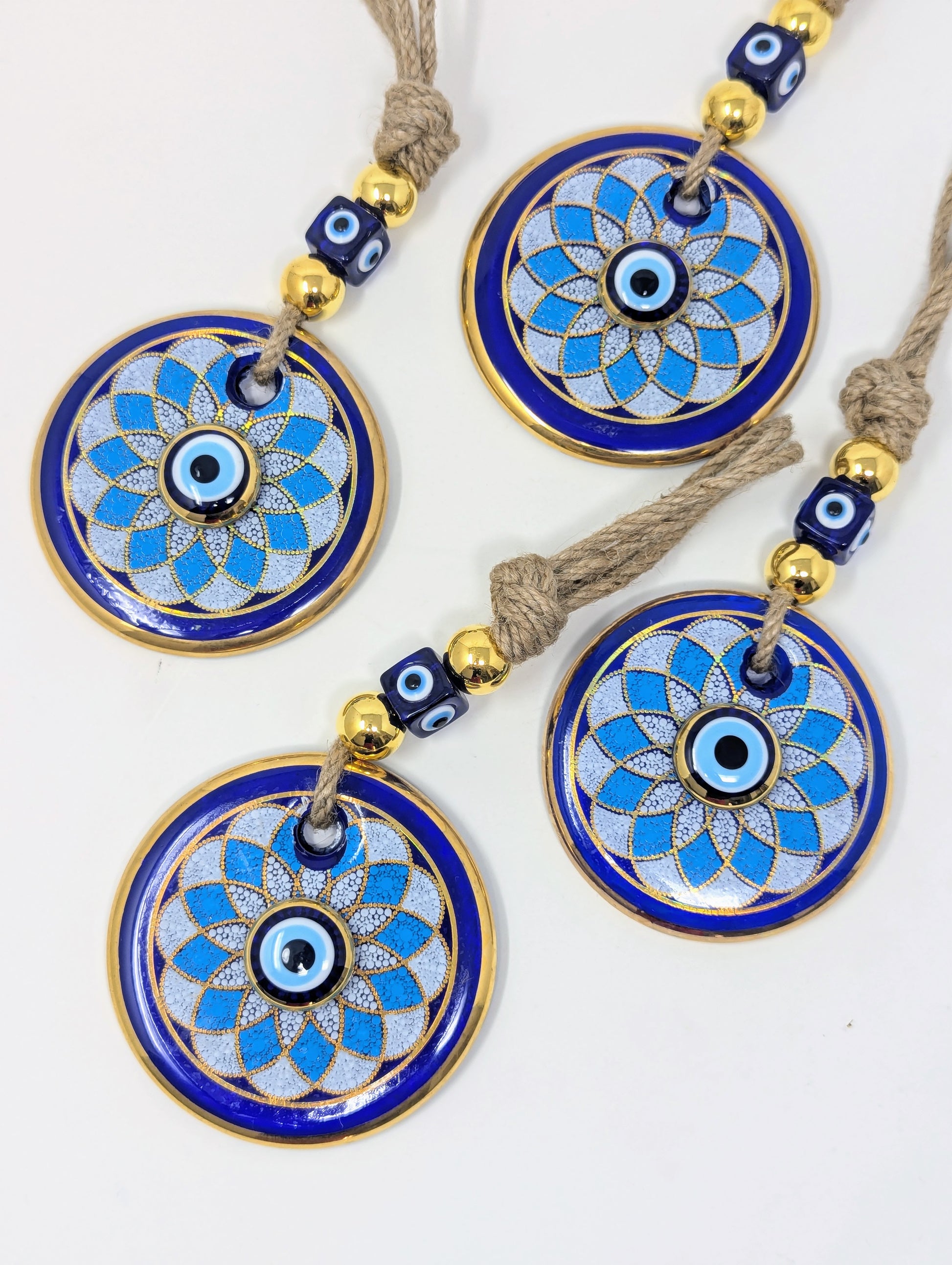 Three matching circular evil eye wall hanging with blue and white enamel patterns, gold-plated borders, and brown cord tassels, displayed on a white background.