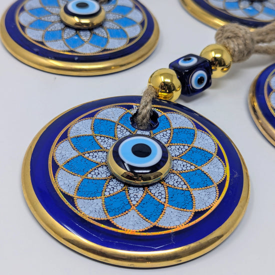 Blue and gold circular evil eye wall hanging ornaments with decorative beads on a light gray background.