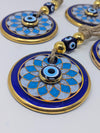 Blue and gold circular evil eye wall hanging ornaments with decorative beads on a light gray background.