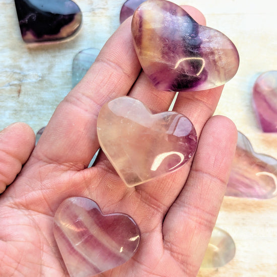 Rainbow fluorite Heart-shaped translucent stones held in a hand with a blurred background
