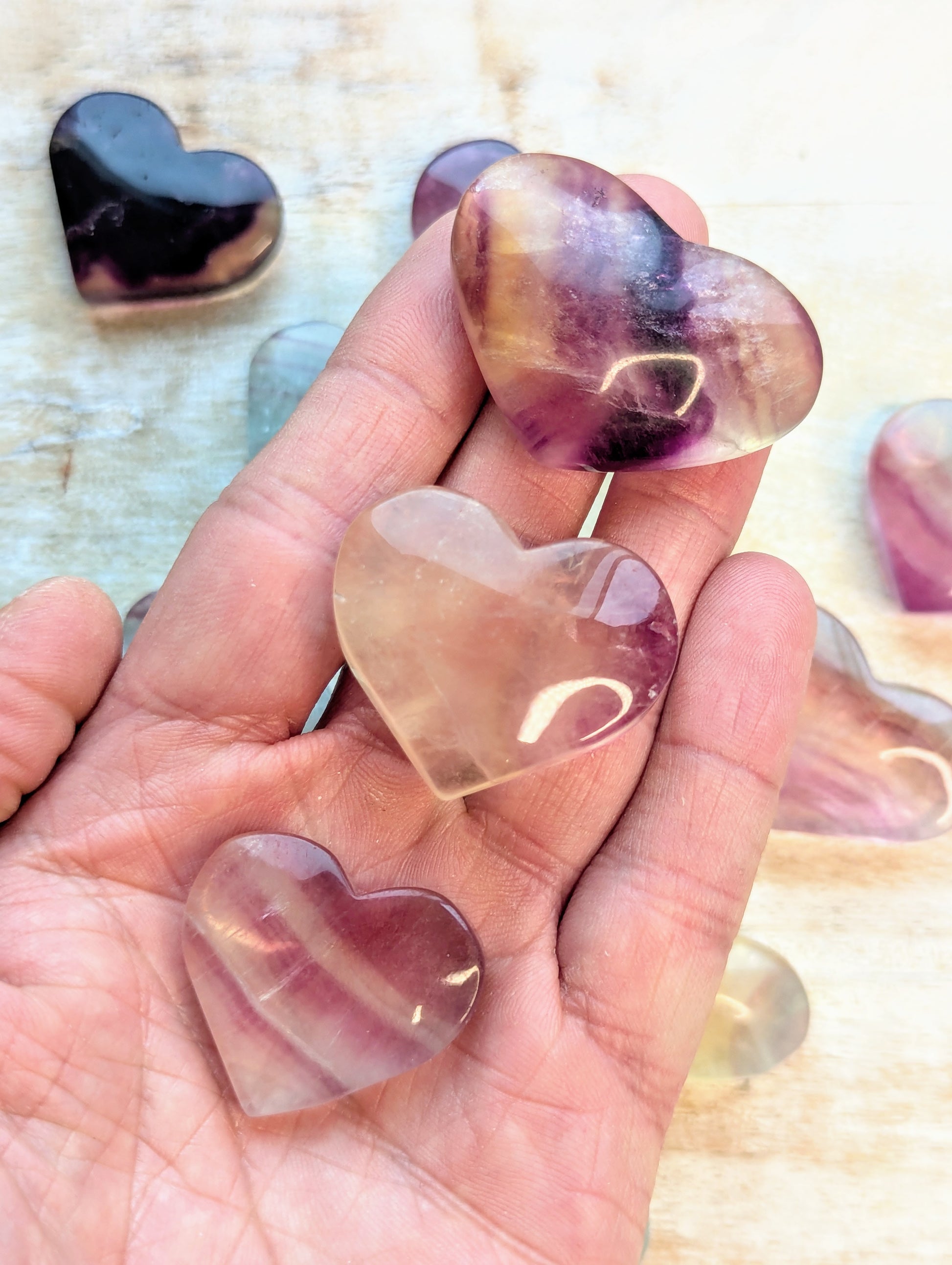 Rainbow fluorite Heart-shaped translucent stones held in a hand with a blurred background