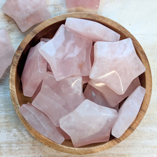 Rose quartz crystal stars carving in a wooden bowl on a light wooden surface