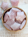 Rose quartz crystal stars carving in a wooden bowl on a light wooden surface