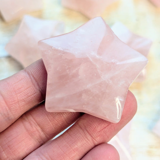 Star-shaped rose quartz crystal held between fingers against a blurred background