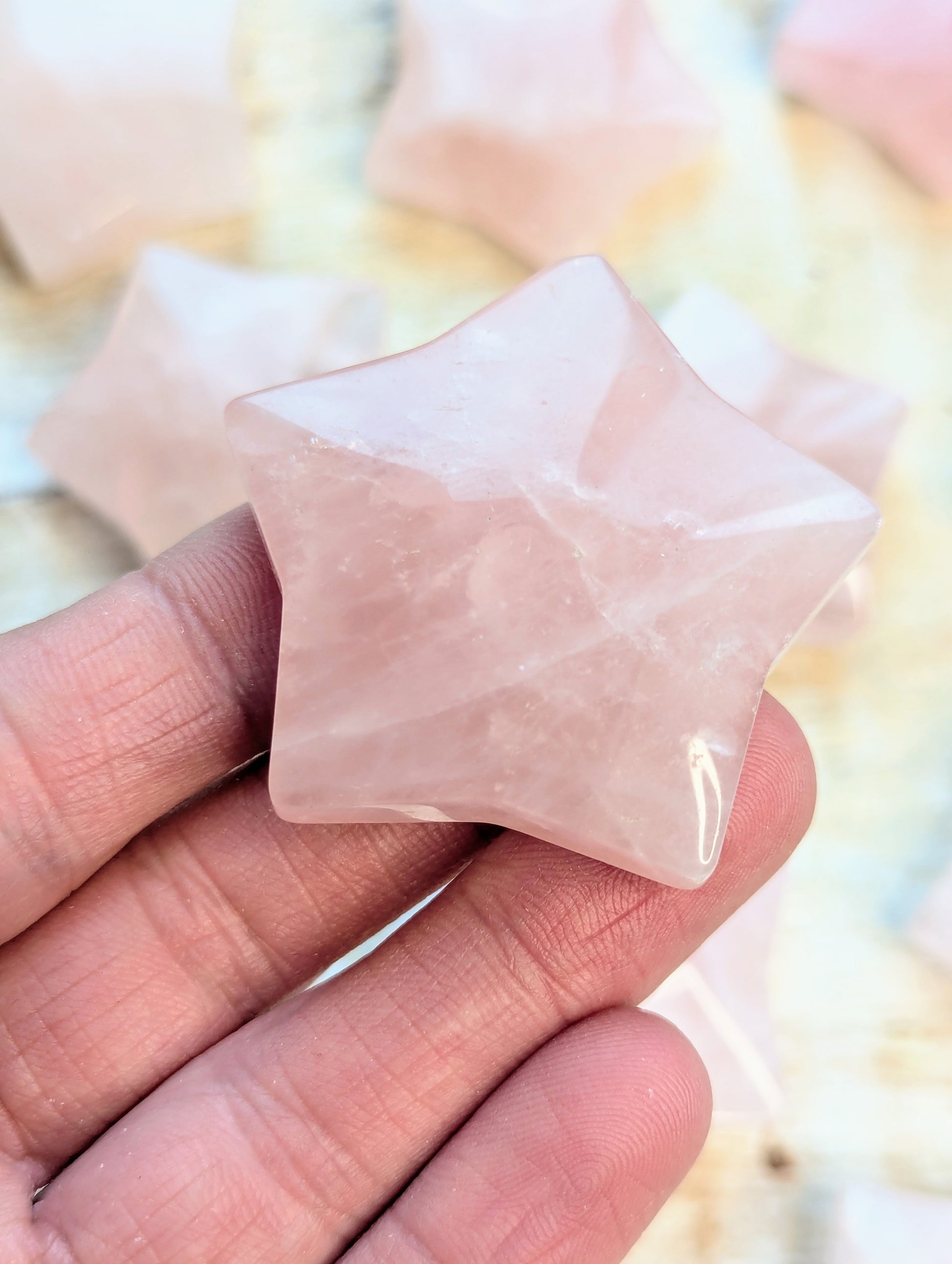 Star-shaped rose quartz crystal held between fingers against a blurred background