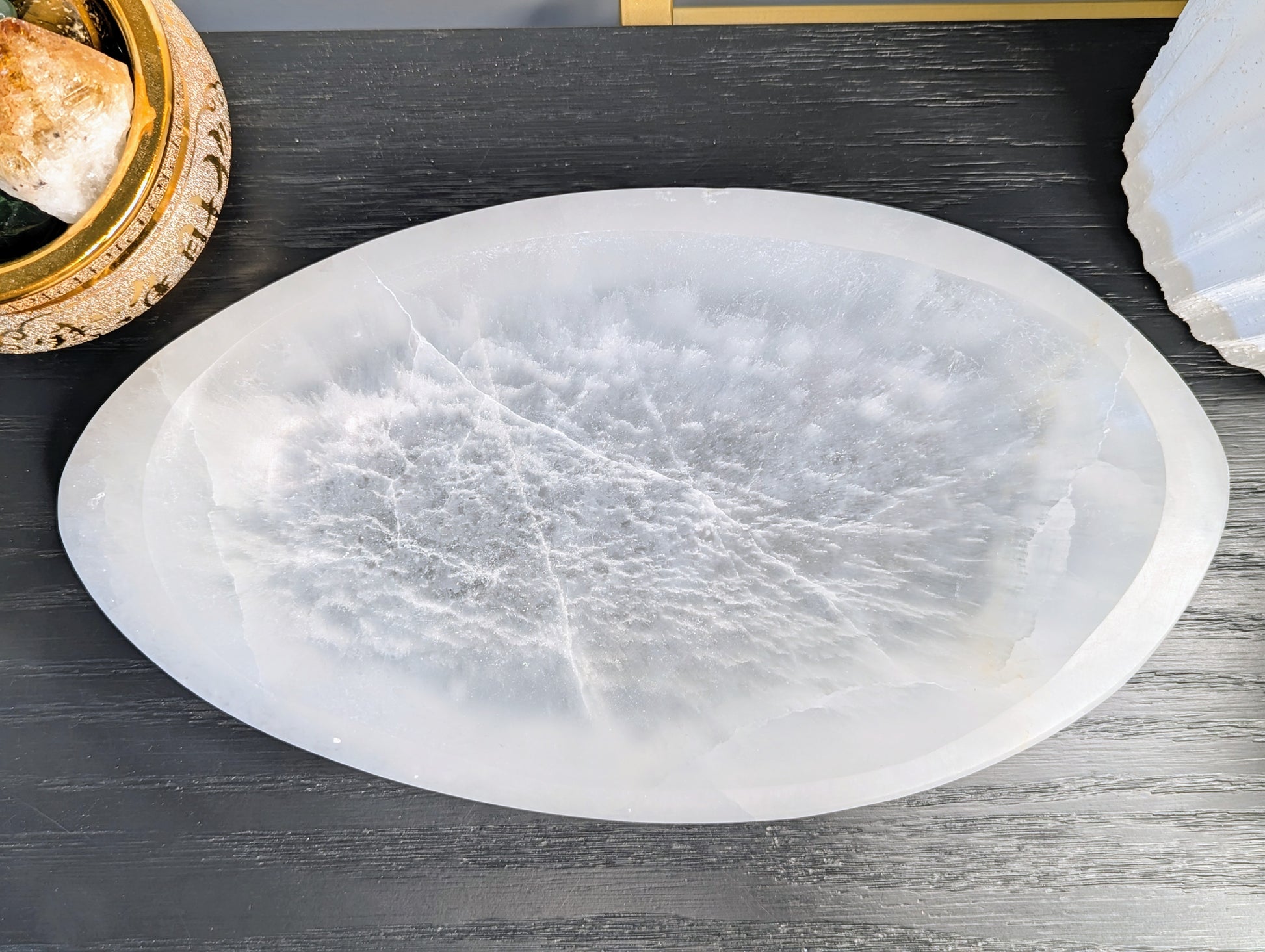 An oval extra large selenite bowl with natural crystalline textures, displayed on a dark gray wood surface.