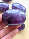 Purple gemstone held in a hand with a blurred background