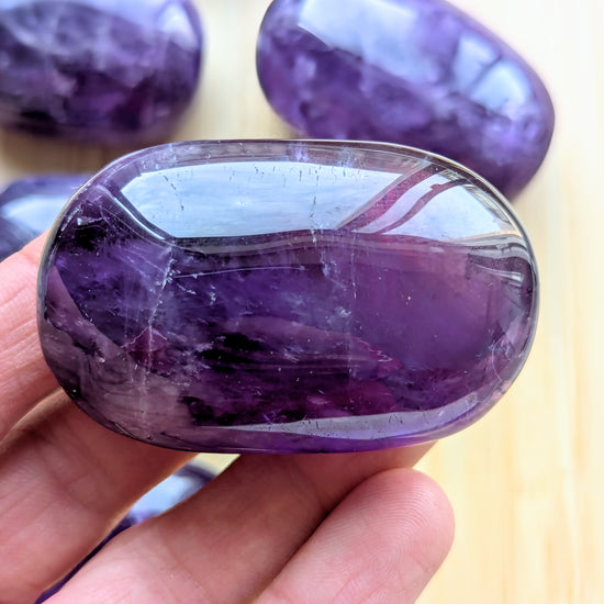 Purple gemstone held in a hand with more gemstones in the background