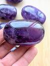 Purple gemstone held in a hand with more gemstones in the background