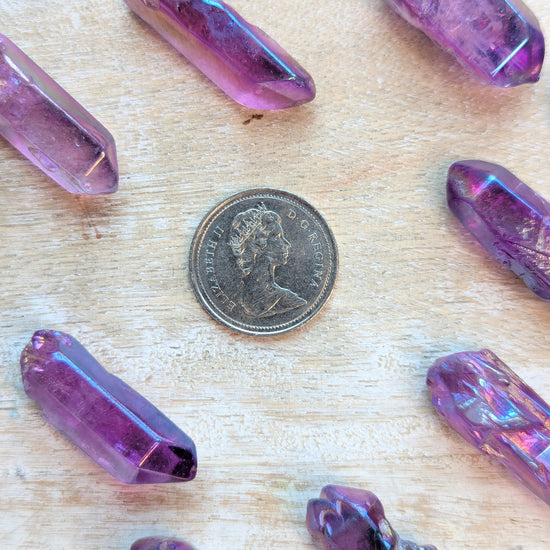 Angel Aura Purple crystal-like objects on a wooden surface with a coin for scale.