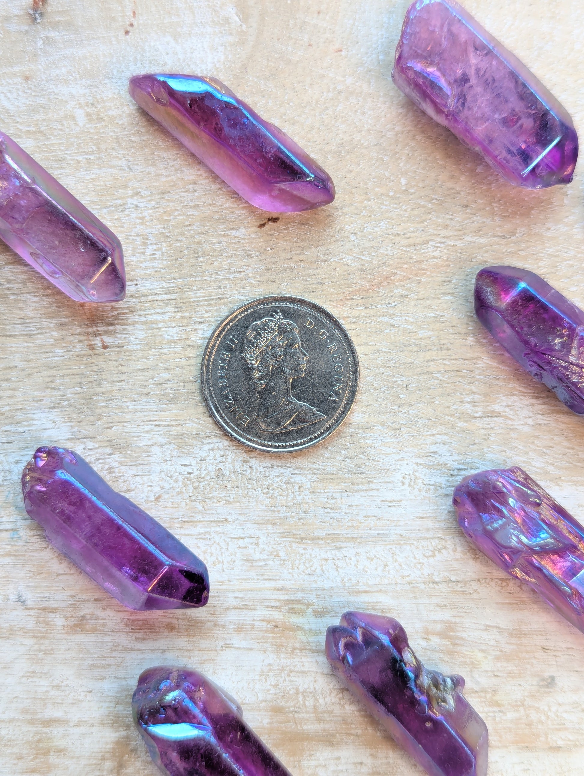 Angel Aura Purple crystal-like objects on a wooden surface with a coin for scale.