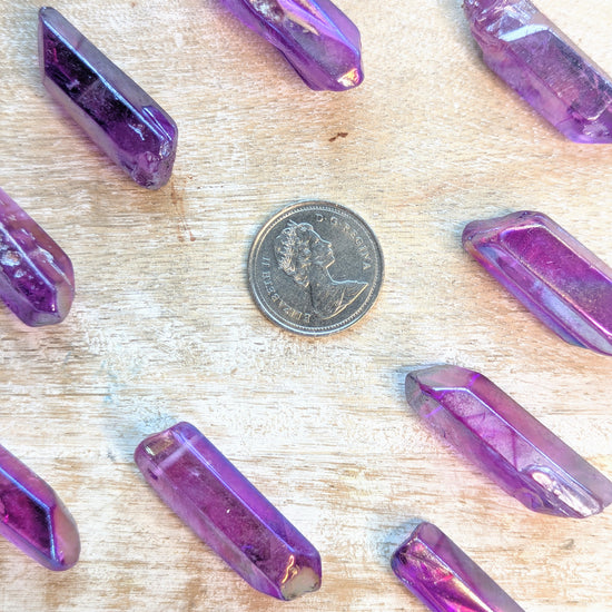 Angel aura Purple crystal  point on a wooden surface with a coin for scale.