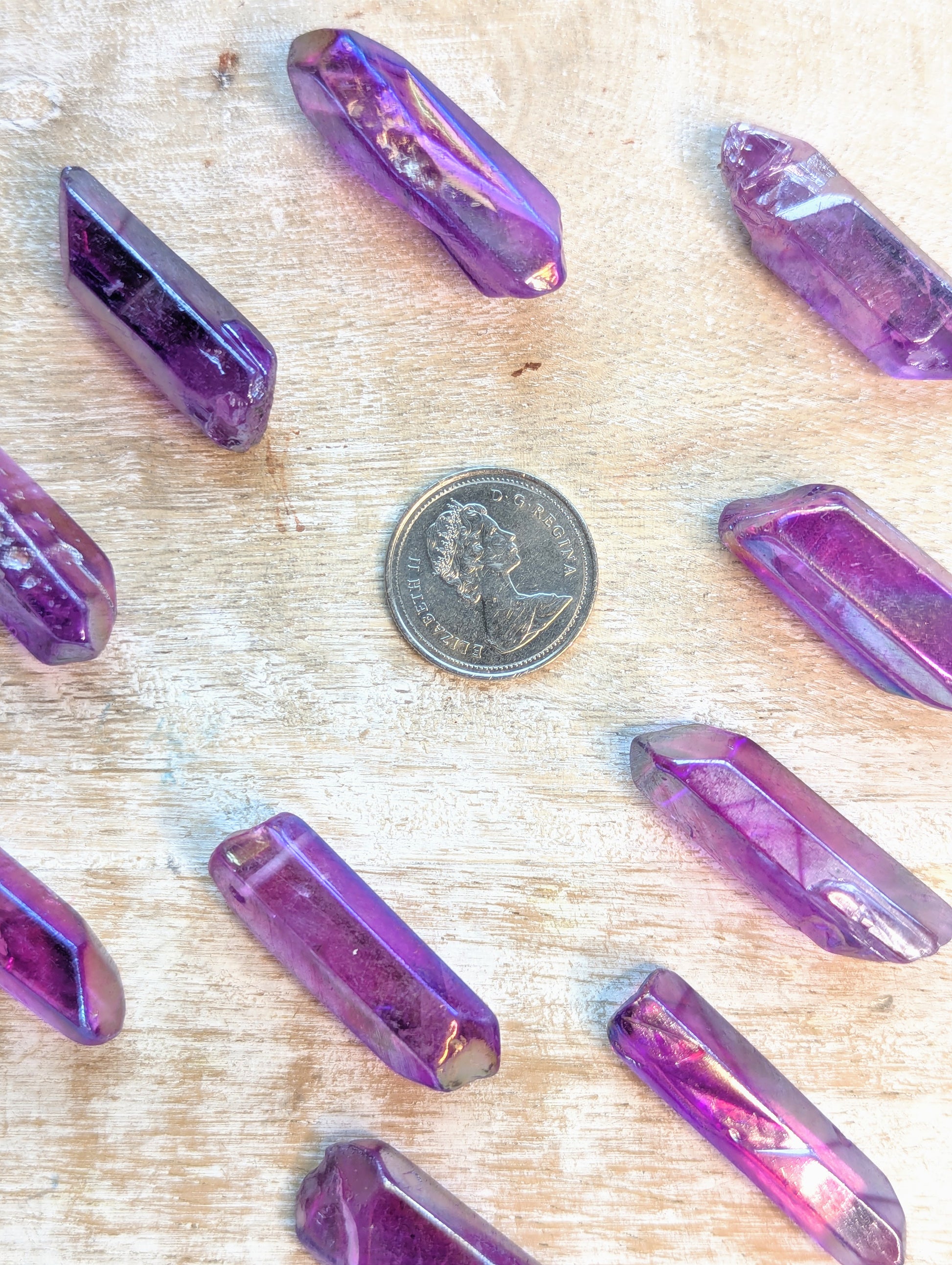 Angel aura Purple crystal  point on a wooden surface with a coin for scale.